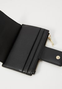 Portafoglio in pelle nera con diversi scomparti per carte di credito, comparto con zip e accessori in tono oro. Texture liscia e design compatto.