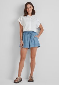 White short-sleeve button-up shirt with eyelet detail, paired with light blue drawstring shorts and metallic sandals, set against a plain background.