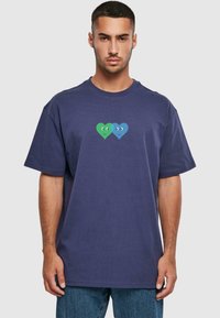 Marineblå oversized t-shirt lavet af bomuld, med to tegneserie hjerte designs, et grønt og et blåt, begge med enkle ansigtsudtryk.