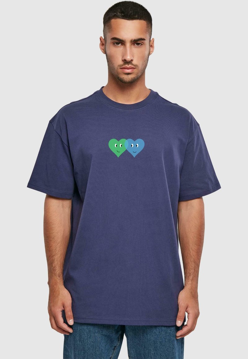Marineblå oversized t-shirt lavet af bomuld, med to tegneserie hjerte designs, et grønt og et blåt, begge med enkle ansigtsudtryk.