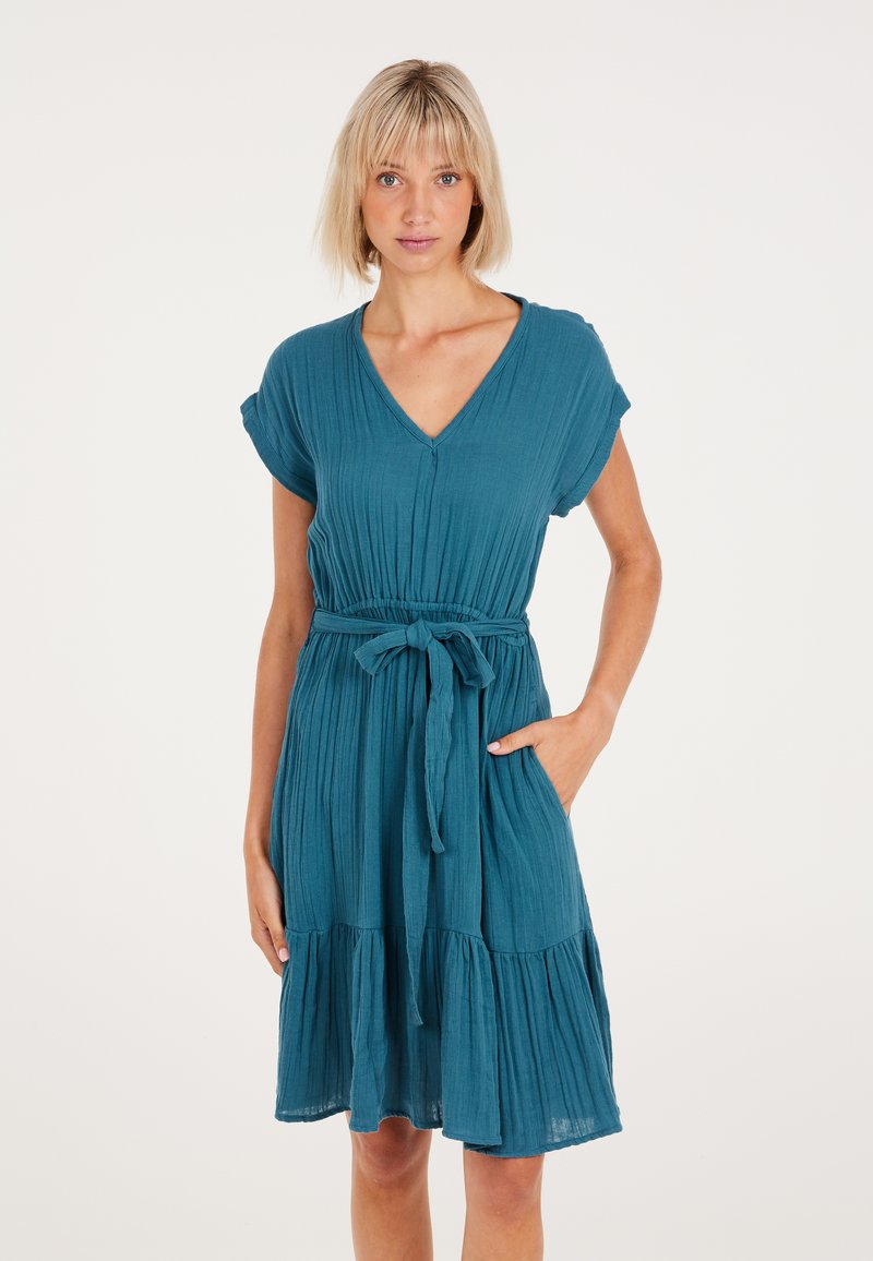Teal, korte mouwen jurk van gekreukt materiaal. Heeft een diepe V-hals, een taille met strik, en een uitlopende, gelaagde rok. Inclusief zakken.