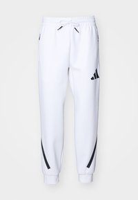 Bílé tepláky s elastickým pásem a stahovací šňůrkou, se černými bočními pruhy a logovými akcenty na obou stranách. Měkký texture, zúžený střih.