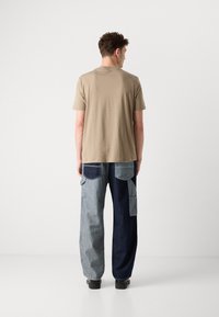 Beige bomulds t-shirt parret med løstsiddende, patchwork denim bukser i lys og mørkeblå, med flere lommer. Sorte sko.