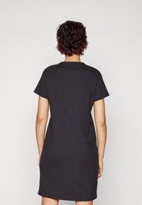 Vestido negro de canalé con mangas cortas, cuello redondo y un corte relajado, que presenta un diseño básico sin patrones ni acentos adicionales.