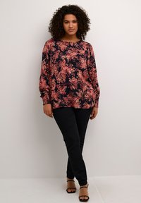 Blouse à manches longues à fleurs marine avec des motifs roses et corail, associée à un pantalon noir slim et des sandales à lanières noires.