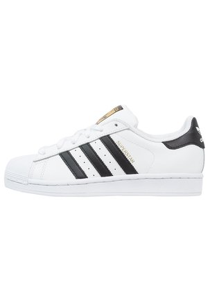Biały sneaker Adidas Superstar z czarnymi paskami, noskiem typu shell toe i złotym napisem "Superstar" po boku.