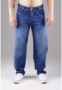 Blaue Jeans im relaxed Fit mit ausgewaschenen Frontpaneelen, fünf Taschen und kupferfarbenen Nieten. Kombiniert mit weißen Sneakers.