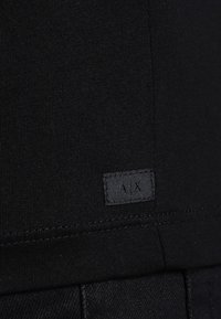 Sort bomulds T-shirt med ribbet tekstur, der har et lille stofmærke med "AX" nederst på kanten.