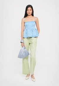 Top peplum bleu deschis din material texturat, asociat cu pantaloni largi de un verde pal. Ținând o geantă din satin bleu deschis, purtând pantofi cu toc bloc crem.