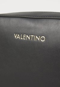 Sac en cuir noir avec une texture lisse, détail du logo doré "Valentino" et coutures discrètes le long des bords.