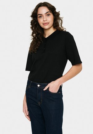 Zwart kortemouwen poloshirt met een kraag en knopenlijst, gecombineerd met donkerblauwe denim jeans met zichtbare stiksels en een voorzak.