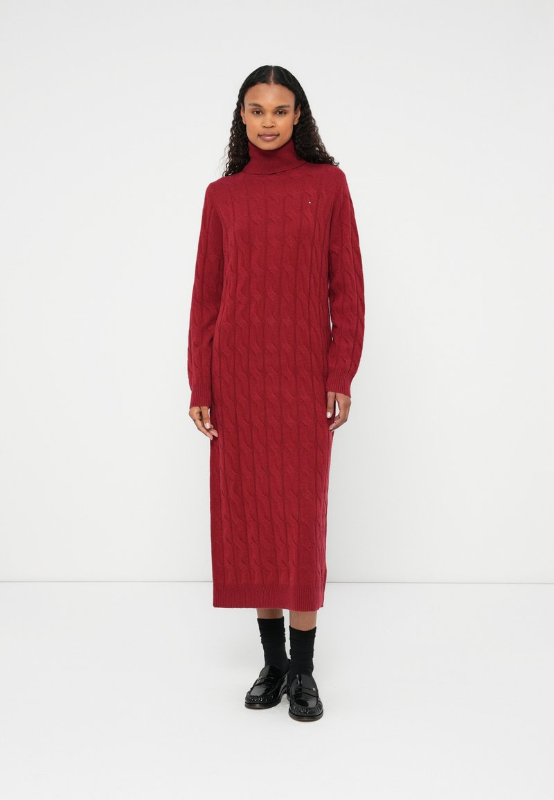 Abito rosso lavorato a maglia con motivo a trecce, colletto alto e maniche lunghe; design lungo abbinato a accessori neri.