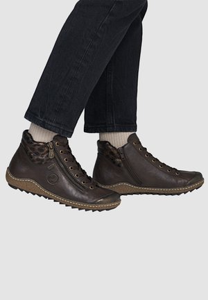 Brune læderankelstøvler med sidelommer og snørebånd, båret med lyse beige sokker og sorte bukser.