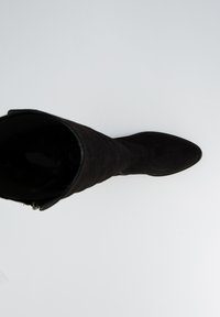 Bota de ante negra hasta la rodilla con punta afilada, textura suave y un detalle de cremallera a lo largo del lado. El interior es brillante y oscuro.