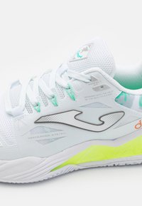 Zapatilla deportiva blanca con parte superior de malla, acentos turquesa y logo gris. Presenta una suela amarilla y detalles del sistema de ventilación.