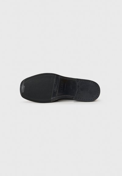 Semelle de chaussure en cuir noir avec un grip texturé, présentant une forme arrondie et des détails perforés le long du bord. Finition propre et lisse.
