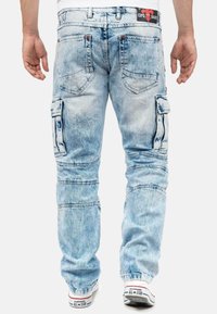 Light blue denim cargo pants with multiple pockets, stitched details, and a relaxed fit, paired with white Converse sneakers.