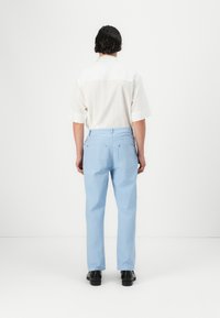 Ανοιχτό μπλε παντελόνι slim fit, κατασκευασμένο από λείο ύφασμα. Διαθέτει δύο πίσω τσέπες και διακριτικές μπλε λεπτομέρειες. Φοριέται με λευκή κοντομάνικη μπλούζα.