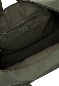 Interieur van een open olijfgroene tas met stoffen voering, een ritssluitingvak en een klein merklapje in het zakgebied.