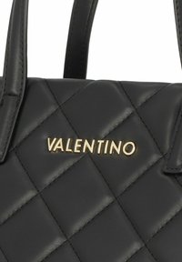 Juodas išklotinis odinis rankinės modelis su viršutinėmis rankenomis ir ryškiu auksiniu "Valentino" logotipu. Textūruota paviršius su deimanto raštu.