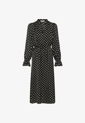Langermet svart kjole med hvite polkadotter. Har krage, frontsplitt og midjesnor. Stoffet har en glatt tekstur.