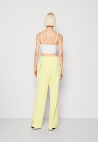 Světle žluté široké kalhoty s hladkou texturou, vysokým pasem a rozparky na lemu, doplněné o přiléhavé bílé crop top.