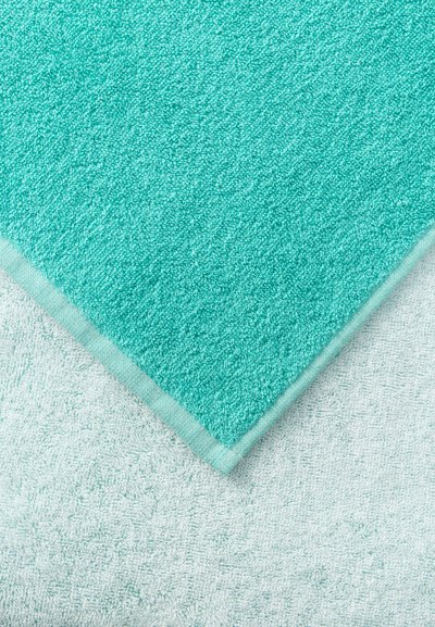 Δύο πετσέτες με απαλή υφή, η μία τυρκουάζ τοποθετημένη διαγώνια πάνω σε μια ανοιχτόγριζη πετσέτα από κάτω.