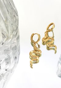 Guldörhängen i form av ormar med intrikata detaljer och en polerad yta, hängande från hoops; reflekterande bakgrund ger djup.