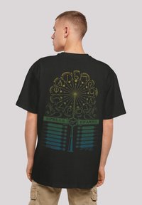 Černé tričko s barevným potiskem kouzel a zaříkadel, se složitými symboly a textem v zelené a žluté na zadní straně.