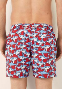 Bañador rojo con un patrón repetido de tiburones azules. Cuenta con una cinturilla elástica y un corte relajado, adecuado para actividades acuáticas.