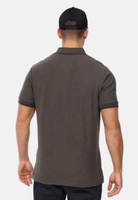 Polo marrón de manga corta, con cuello acanalado y detalles en rojo. La tela parece suave con un corte clásico.
