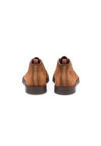 Bottines en suède marron avec une texture lisse, bout rond et design minimaliste. Elles possèdent une semelle en caoutchouc noir et un onglet arrière renforcé.