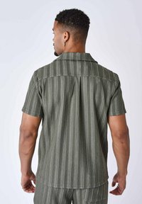 Camicia a maniche corte verde a righe con colletto a punta, realizzata in un tessuto strutturato e con righe bianche verticali, yoke posteriore con bottoni.