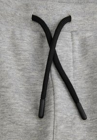 Szare dresowe spodnie z tkaniny, mające stadionowy pas z żeberkami i czarną sznurówkę, o teksturowanej powierzchni i czarnych plastikowych końcówkach na końcach.