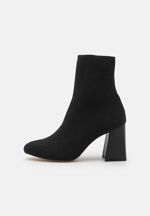 Zwarte enkelboots van zacht suede, met een spitse neus en een robuuste, rechthoekige hak. Het ontwerp bevat minimale stikdetails.