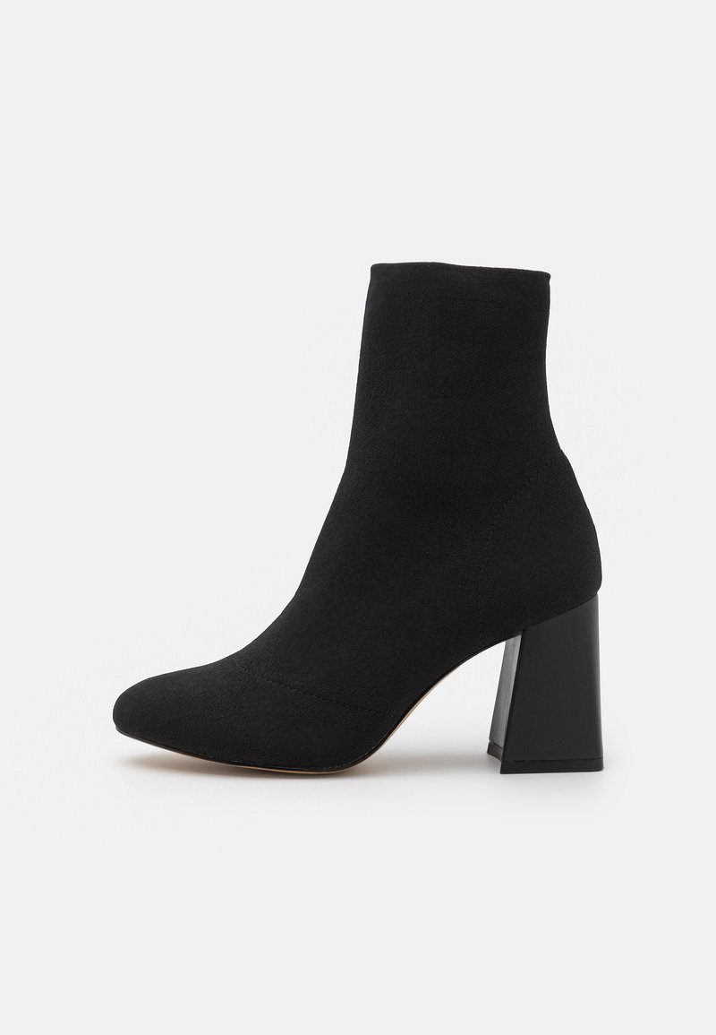 Schwarze ankle boots aus weichem Wildleder, mit einer spitzen Zehenform und einem klobigen, rechteckigen Absatz. Das Design umfasst minimale Stickdetails.