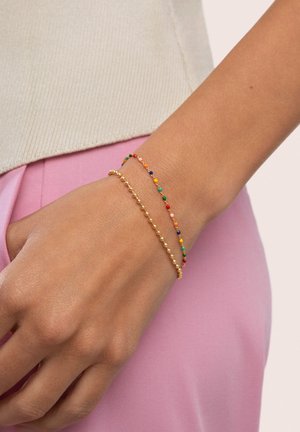 Pulseras de oro y de cuentas multicolores en una muñeca. La pulsera de oro presenta pequeñas cuentas redondas, mientras que la otra tiene colores vibrantes y espaciados.