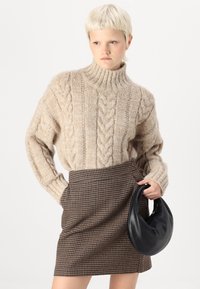 Jersey de cuello alto de punto trenzado en color beige, con puños de canalé, combinado con una falda mini de cuadro de ganso marrón y un bolso de cuero negro.