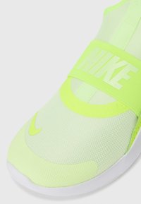 Chaussure de sport Nike avec un dessus en maille jaune néon, une large sangle marquée à mi-pied et une semelle en caoutchouc blanche. Détails de surface texturée visibles.