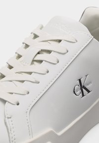 Λευκό αθλητικό παπούτσι Calvin Klein με λευκά κορδόνια και λογότυπο CK στο πλάι, εμφανιζόμενο σε κοντινή γωνία.