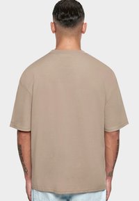 Camiseta de manga corta beige, hecha de un tejido suave, presenta un corte relajado, escote redondo y un detalle de costura visible en el dobladillo.