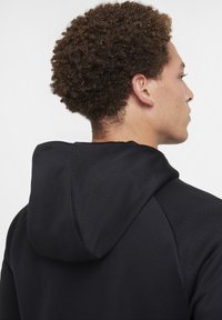 Zwarte hoodie van een gestructureerde stof, met een trekkoordcapuchon, zichtbare naden en een eenvoudig, gestroomlijnd ontwerp.