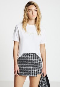 T-shirt blanc à manches courtes avec le mot « élégance » en lettres dorées, associé à une mini-jupe texturée noire et blanche à motifs.