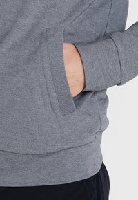 Sudadera gris con un tejido texturizado, que cuenta con un bolsillo lateral. Los puños y el dobladillo son acanalados para mayor refuerzo y ajuste.