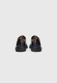 Schwarze Lederschuhe mit abgerundeter Spitze, rückenlosem Design, kontrastierenden weißen Nähten und einer dicken Gummisohle. Das Innenfutter ist hellbraun.