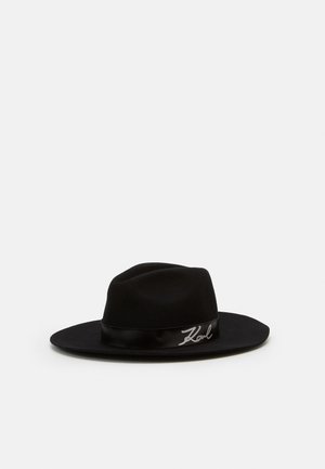Sort bredskygget fedora-hat med et satinbånd, der har en sølvfarvet "Karl"-signatur på en enkel hvid baggrund.