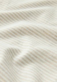 Tissu doux avec de fines rayures horizontales beige et blanches, présentant des plis délicats et une texture lisse.