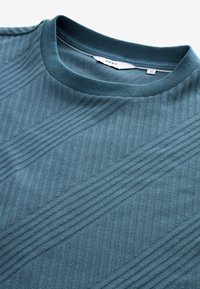 Blå tekstureret crew-neck sweatshirt med ribbet krave, der har diagonale stribemønstre på stoffet. Blødt materiale.