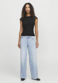 Top nero a maniche corte abbinato a jeans ampi di colore blu chiaro. Tessuto liscio con una morbida consistenza. Design minimalista, senza motivi o accenti visibili.