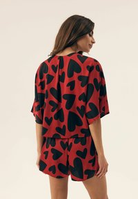 Red outfit with black heart patterns, featuring a loose top with dropped sleeves and matching shorts. Smooth fabric and relaxed fit.